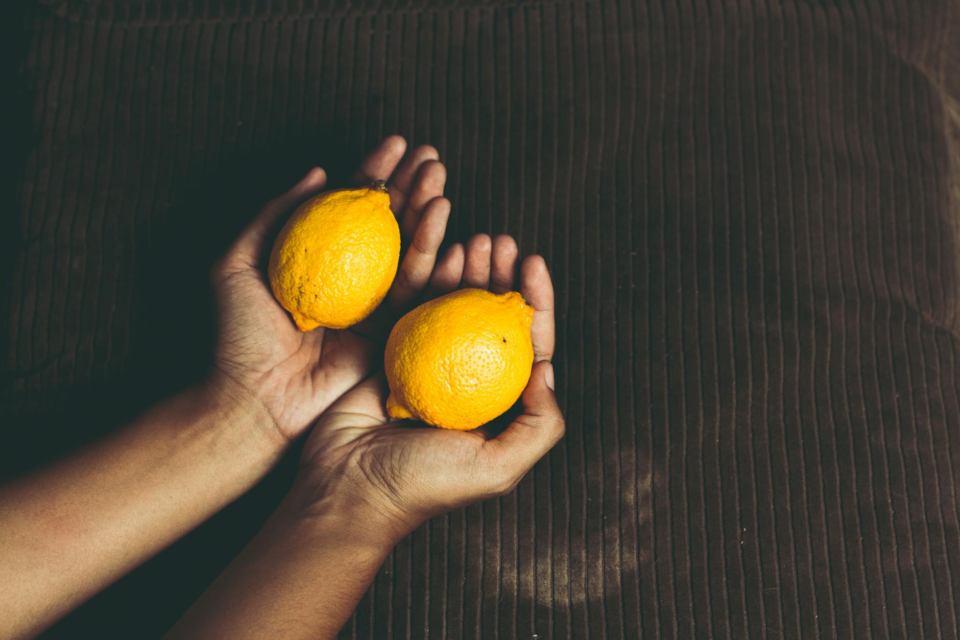 Dos limones frescos sostenidos en las manos sobre una superficie marrón, simbolizando frescura y vitalidad