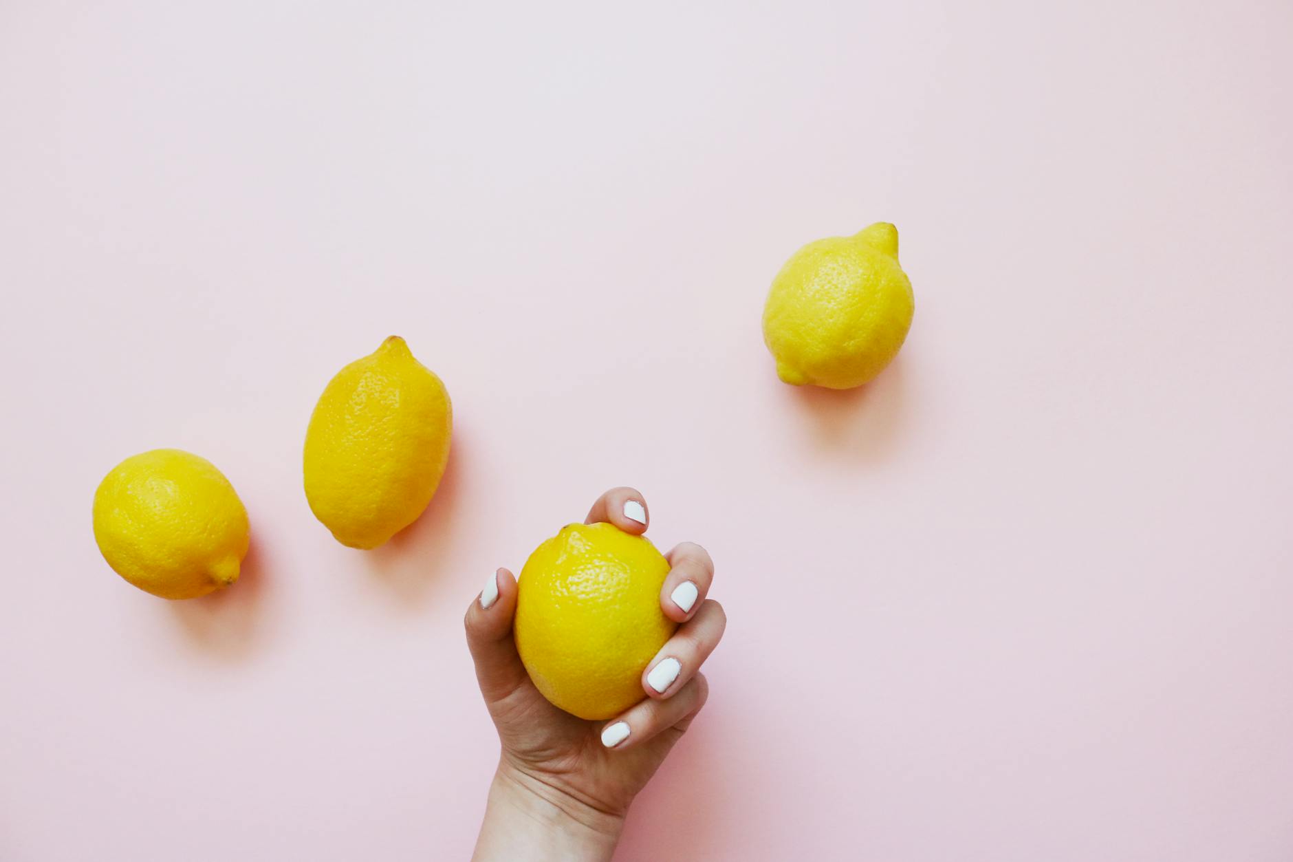 A hand holding a bright lemon against a soft pink background, symbolizing sensitivity and sensation shifts.