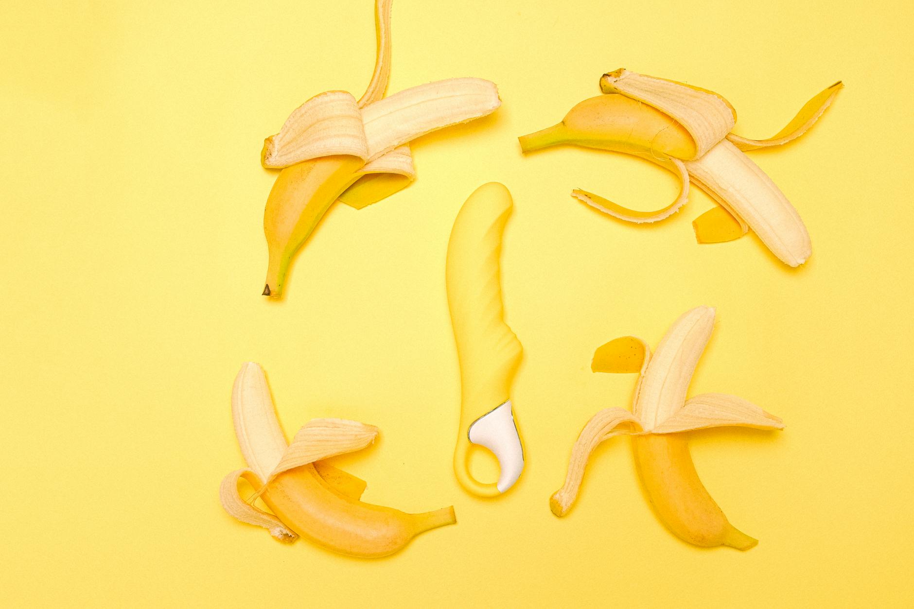 Vibrador de limón amarillo brillante rodeado de limones pelados sobre fondo amarillo pastel