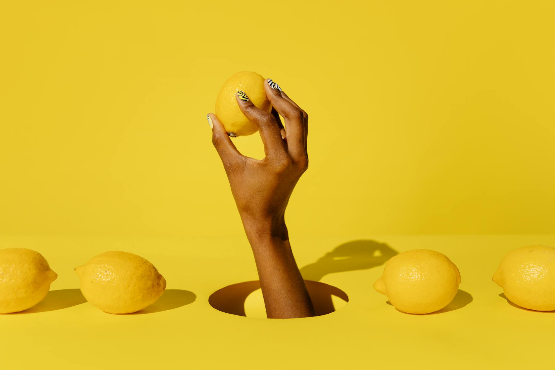 A hand holding a fresh lemon against a bright yellow background