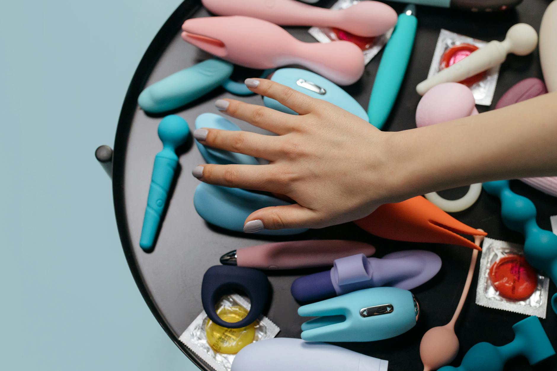 A hand reaching over a variety of colorful sex toys, including lemon vibrators, arranged on a table.