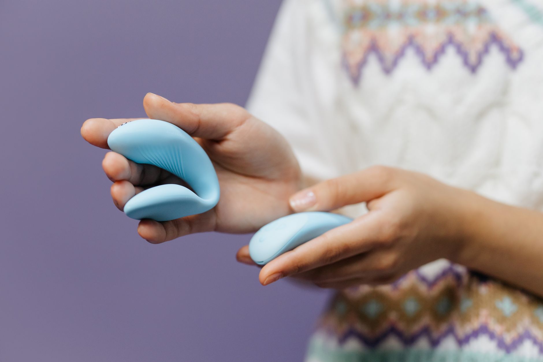 Primer plano de manos sosteniendo un vibrador azul elegante contra un fondo púrpura.