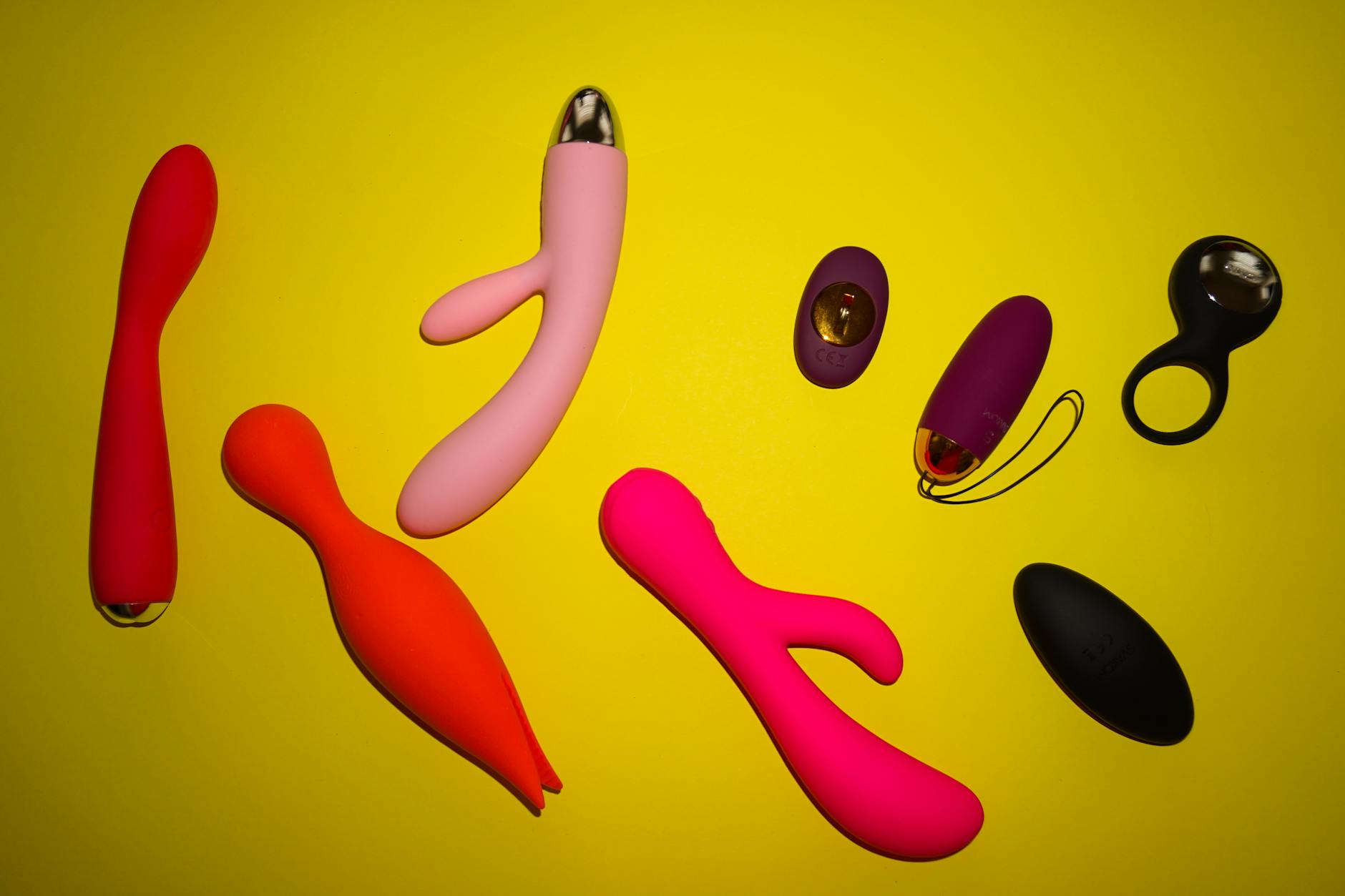 Vibrant collection of colorful sex toys arranged on a bright yellow surface, representing diverse pleasure options
